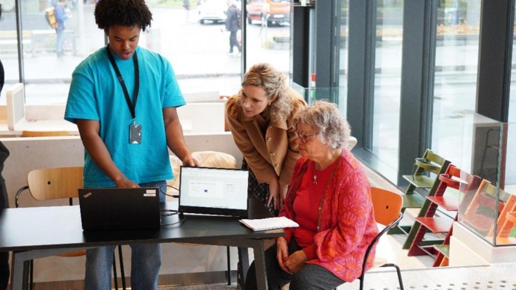 En ung mann og en voksen kvinne og en eldre kvinne ser sammen på en bærbar pc som er slått opp mot de tre. Illustrasjon av veiledningstilbud for digital inkludering