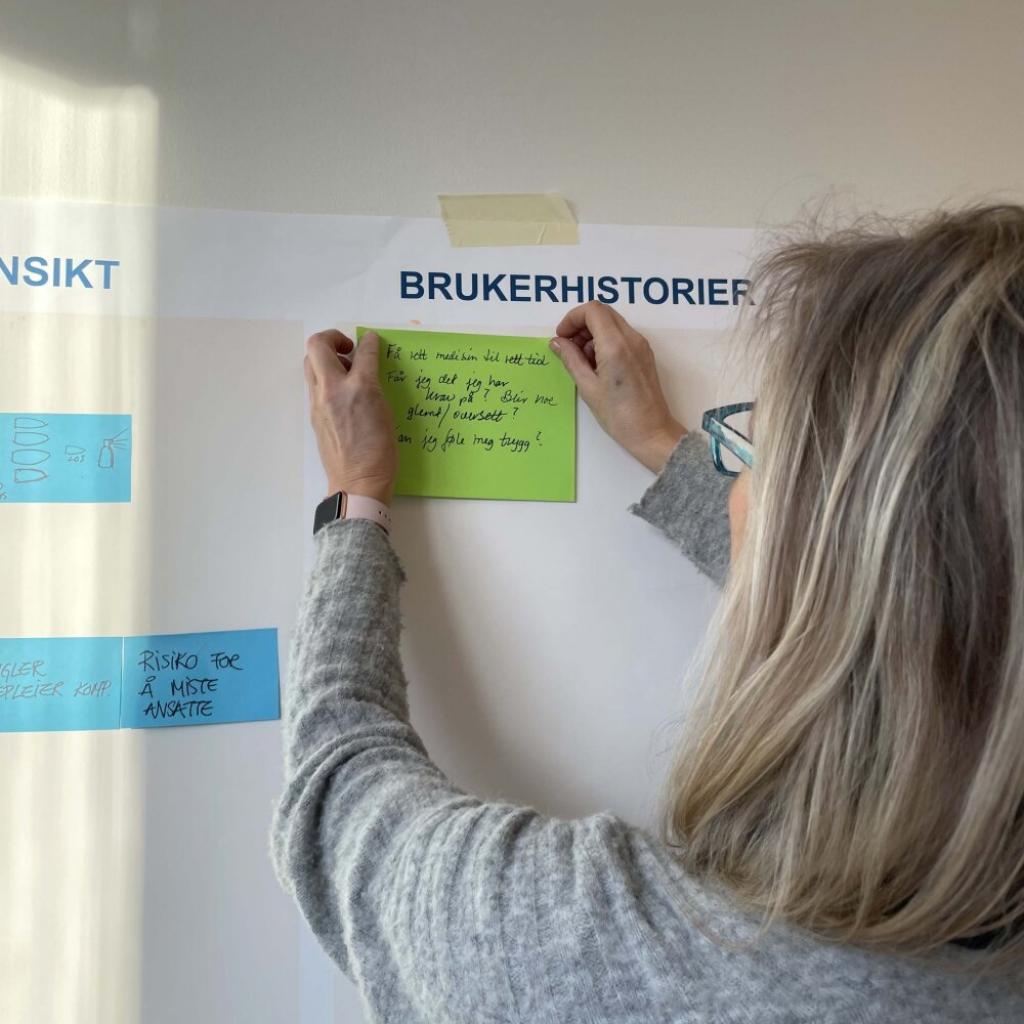 Bilde av prosjektmedarbeider som henger opp post-it på veggen